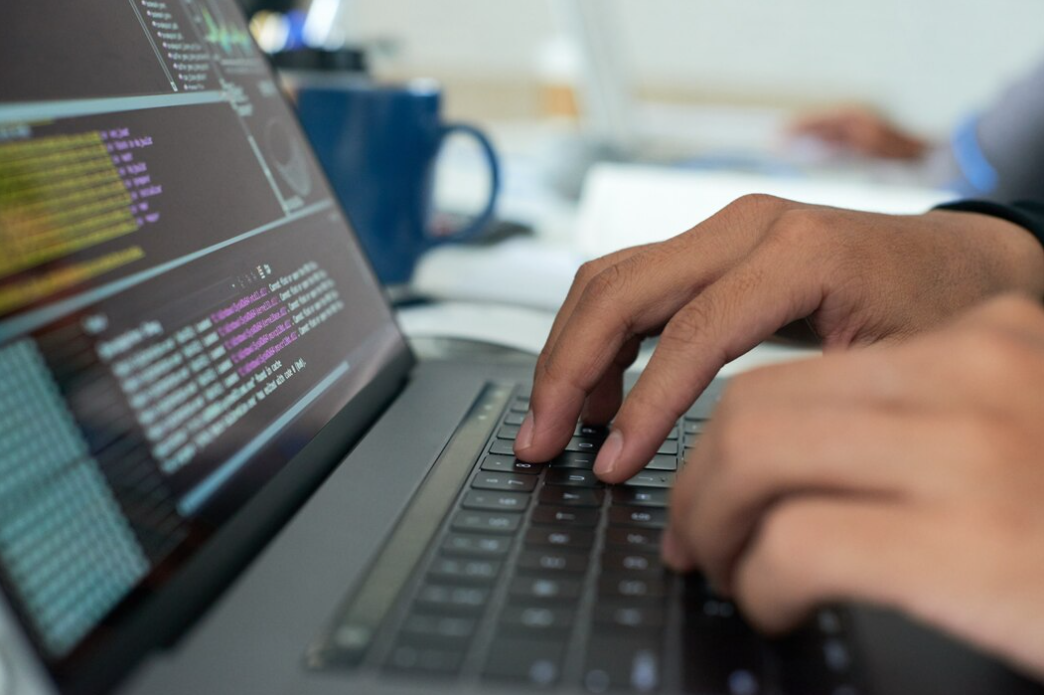 A programmer's hands type swiftly, with code on the laptop screen and a coffee mug nearby